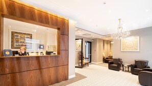 Un área de recepción con un mostrador de madera, una araña de cristal y un espacio de estar con sillones de cuero.