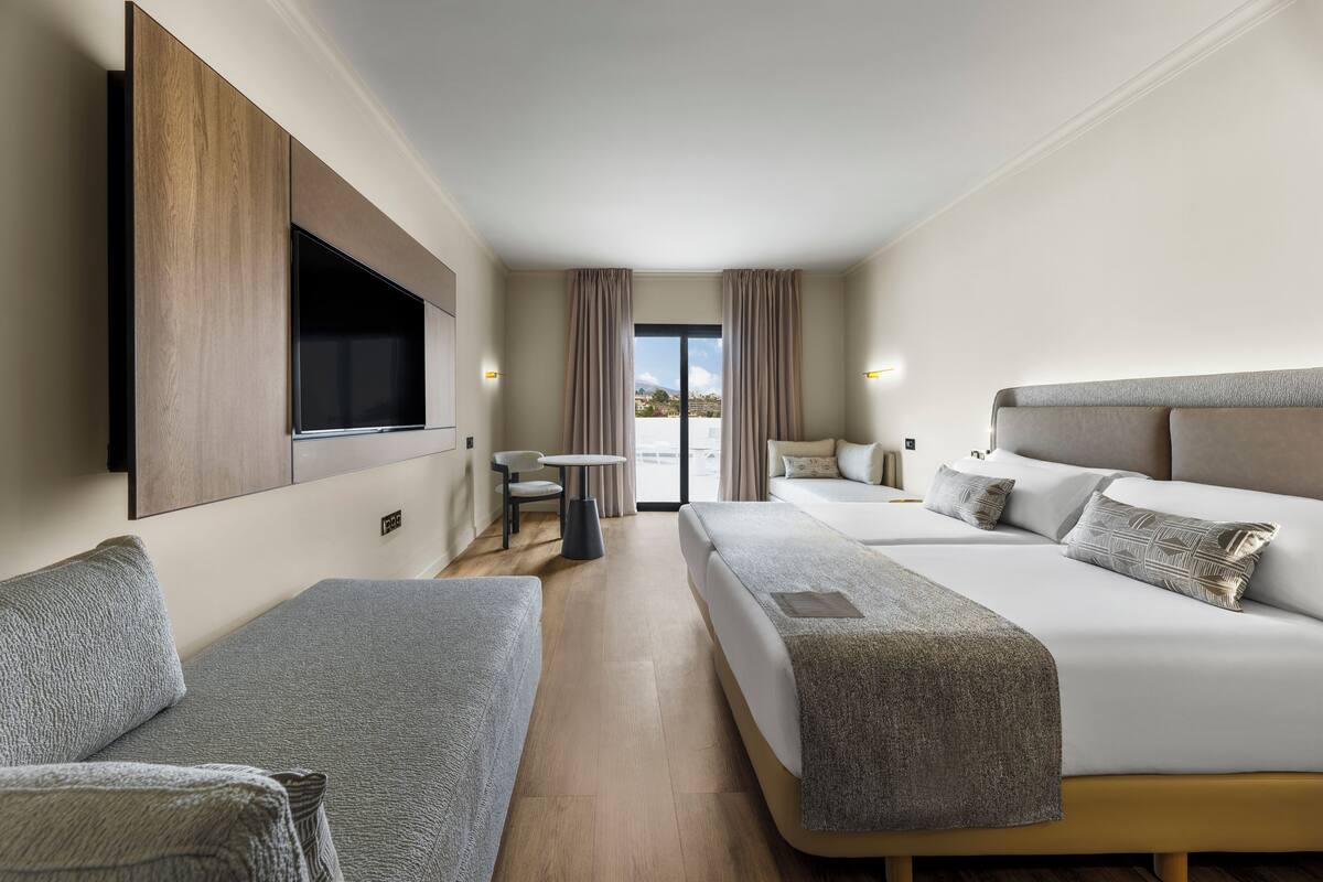 Een hotelkamer met twee bedden, een aan de muur bevestigde televisie, een kleintje tafeltje en uitzicht op het landschap door het raam.