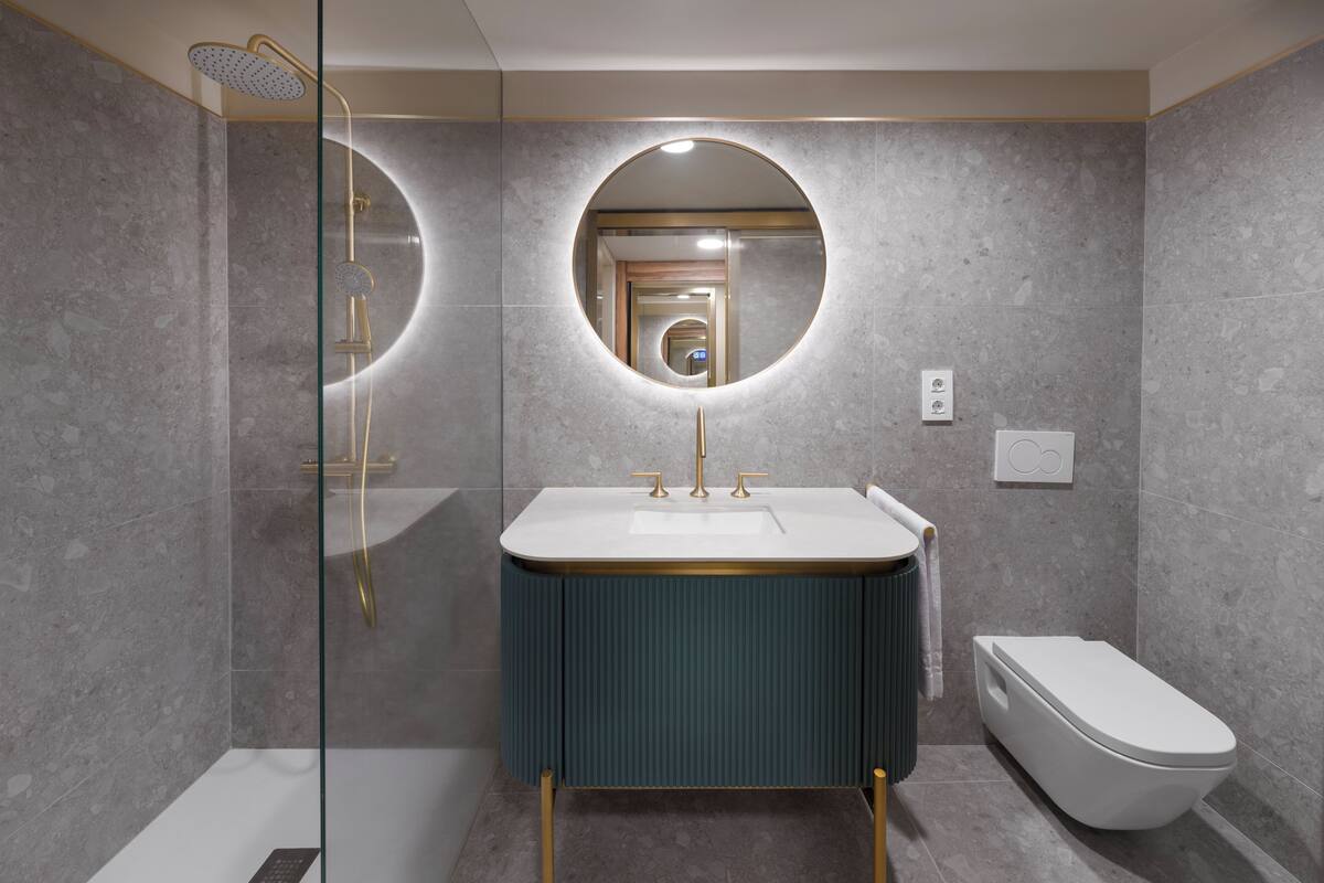 Een moderne badkamer met een douche met glazen wand, een ronde spiegel en een wit toilet.