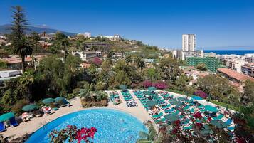 A resort with a large pool, sun loungers, and a view of the ocean and a mountain in the background.