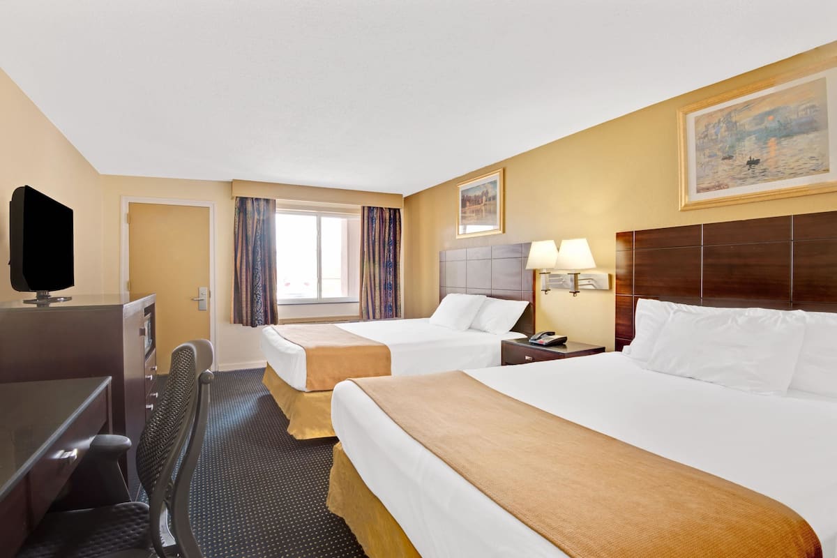 A hotel room with two beds, a desk, a TV, and a window with curtains.