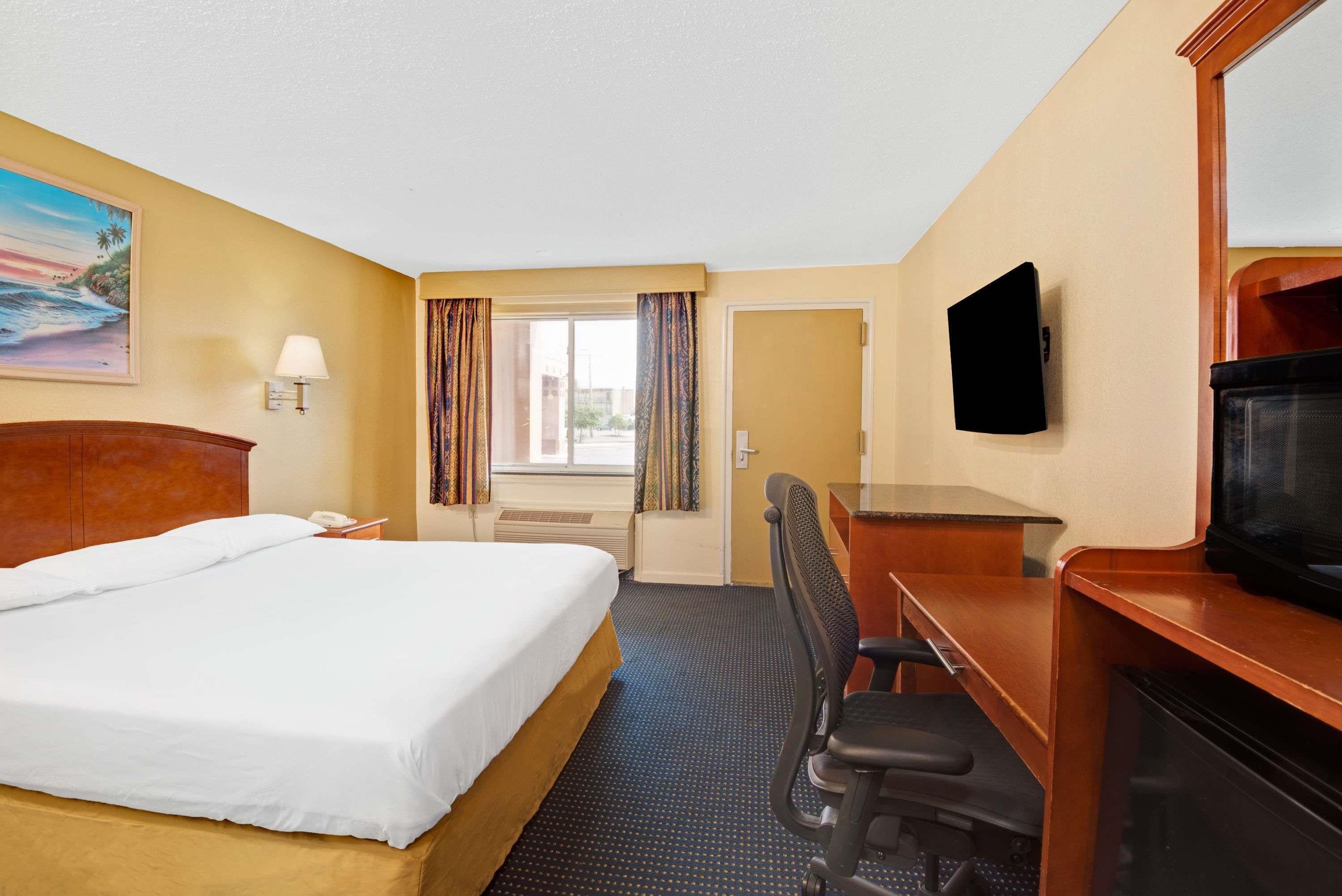 Habitación de hotel con cama, escritorio, silla, televisión y un cuadro en la pared.