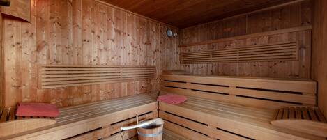 A sauna with wooden benches and a wooden bucket.