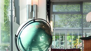 Un globe terrestre posé sur un support, dans une pièce moderne avec un canapé rouge et une grande fenêtre.
