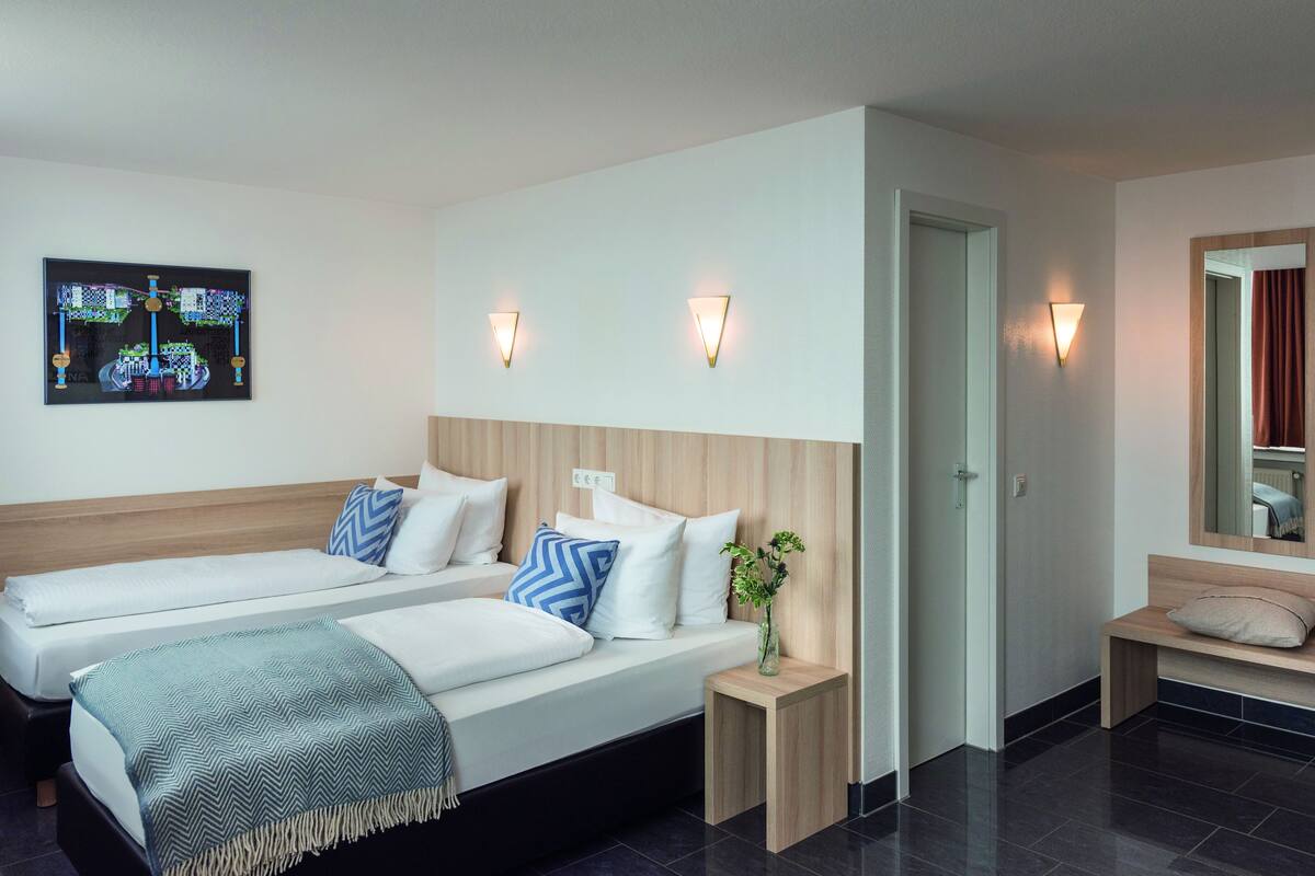 A hotel room with two beds, a bedside table with a vase, and a wall-mounted artwork.