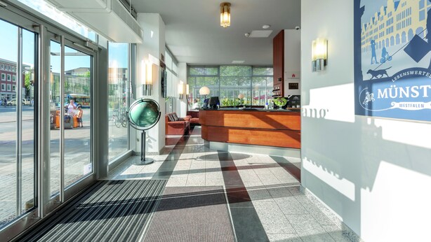 Un hall d’hôtel moderne avec un comptoir d’accueil, de grandes fenêtres et un sol à motifs.