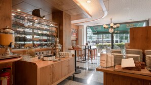 L’intérieur d’un restaurant est décoré de bois, on y trouve une vitrine réfrigérée où sont exposés des plats, ainsi qu’un espace où sont disposées des tables et des chaises.