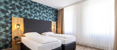 A modern hotel room with two beds, a geometric-patterned wall, and a large window with sheer curtains.
