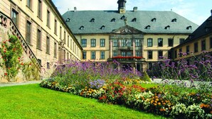 Un bâtiment historique doté d’une cour intérieure, entouré de parterres de fleurs bien entretenus et d’une pelouse parfaitement taillée.