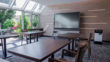 Sala de conferências com uma tela grande, mesas de madeira e cadeiras.