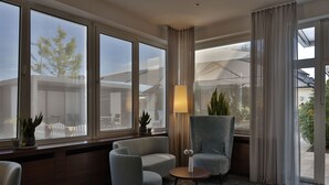 Une chambre d’hôtel avec une grande fenêtre, un canapé, un fauteuil, une petite table et une lampe.