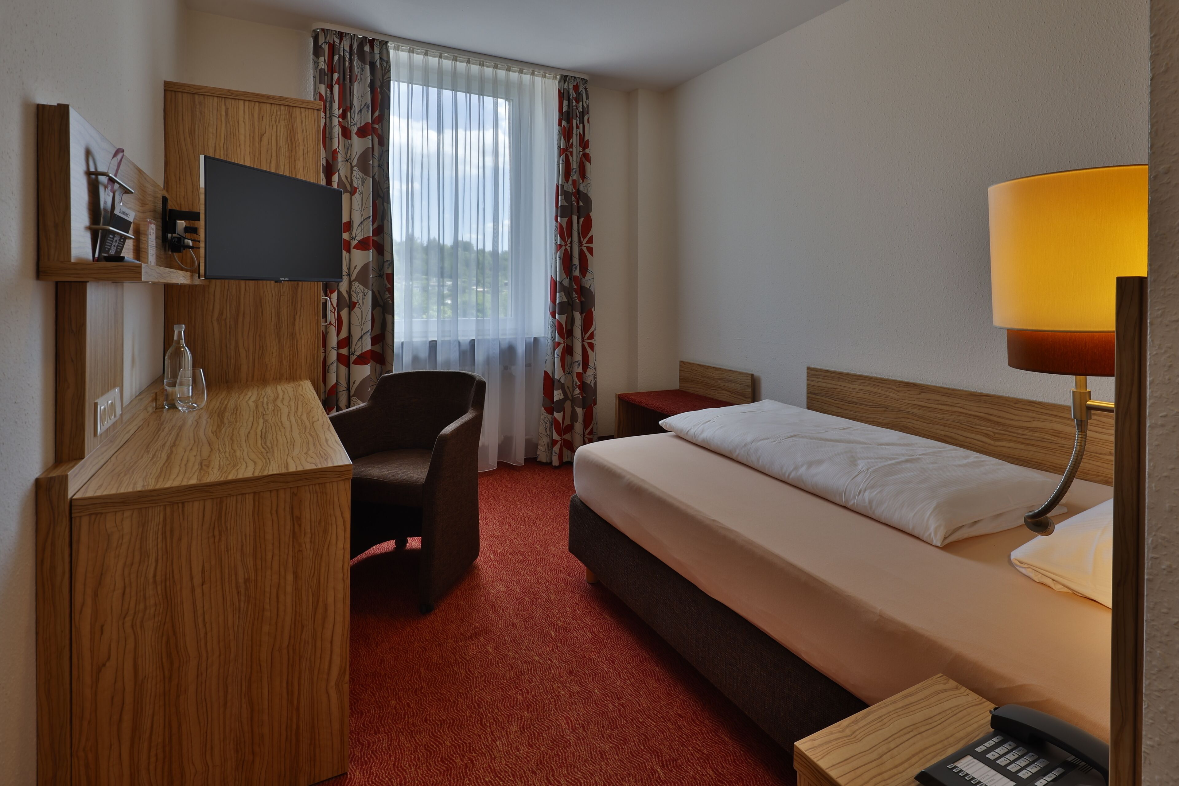 Een hotelkamer met een bed, bureau, stoel, televisie en een lamp.