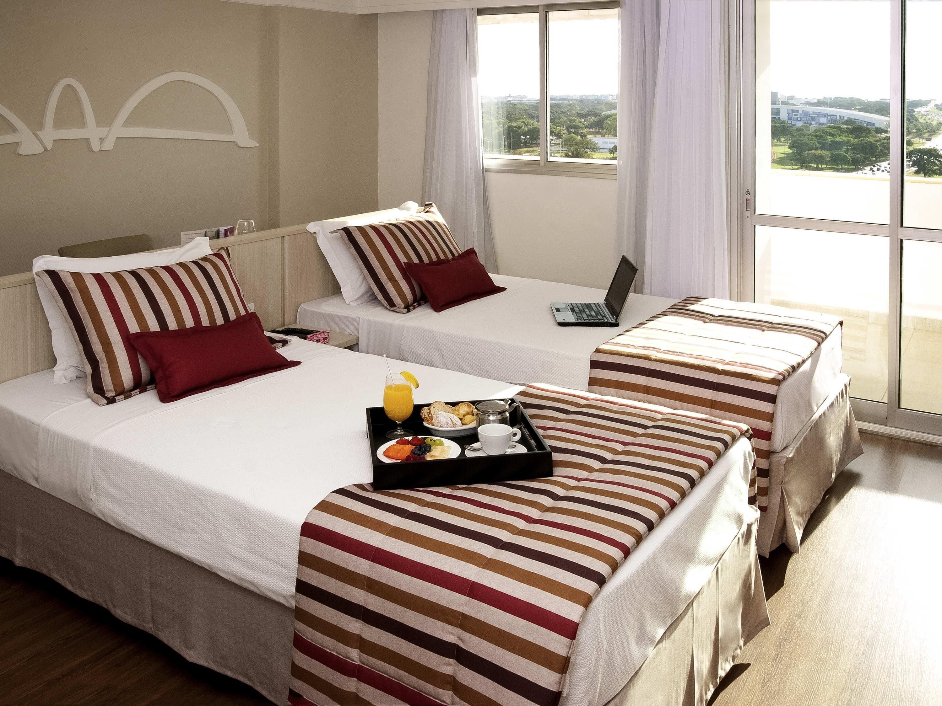 A hotel room with two beds, a laptop on one bed, and a breakfast tray on the other.