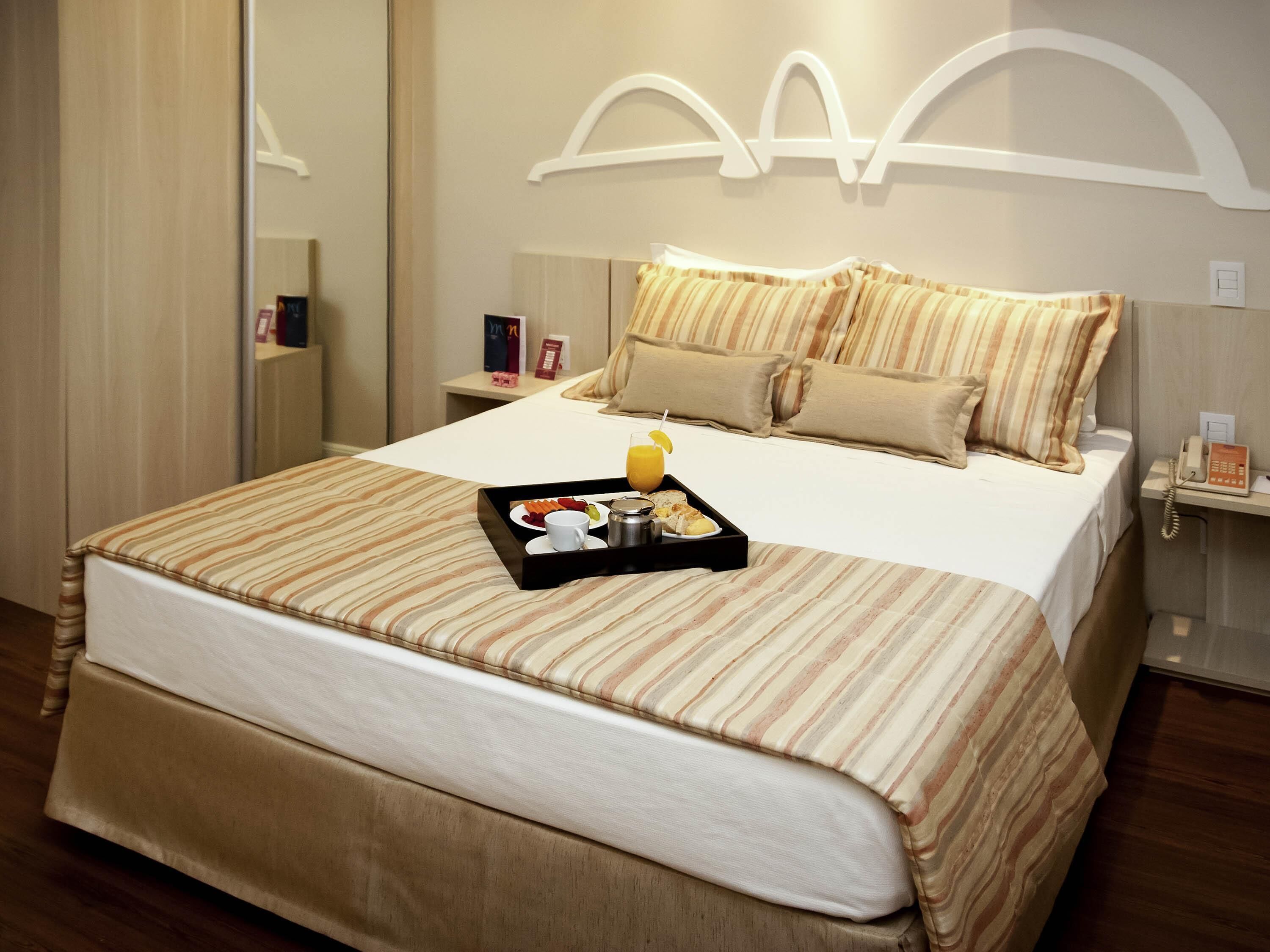 A hotel room with a large bed, a bedside table with a phone, and a tray with breakfast items.