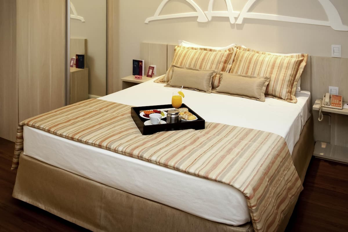 Una habitació d'hotel amb un llit gran, una taula de nit amb un telèfon i un carro amb articles per esmorzar.