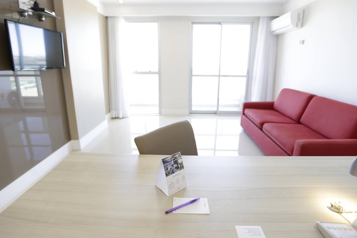 Una sala de estar moderna con un sofá rojo, una mesa de madera con un folleto y un bolígrafo, y un televisor a la izquierda.