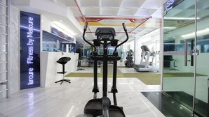 An indoor gym with exercise equipment, a mirrored wall, and a sign reading "Fitness by Merure".