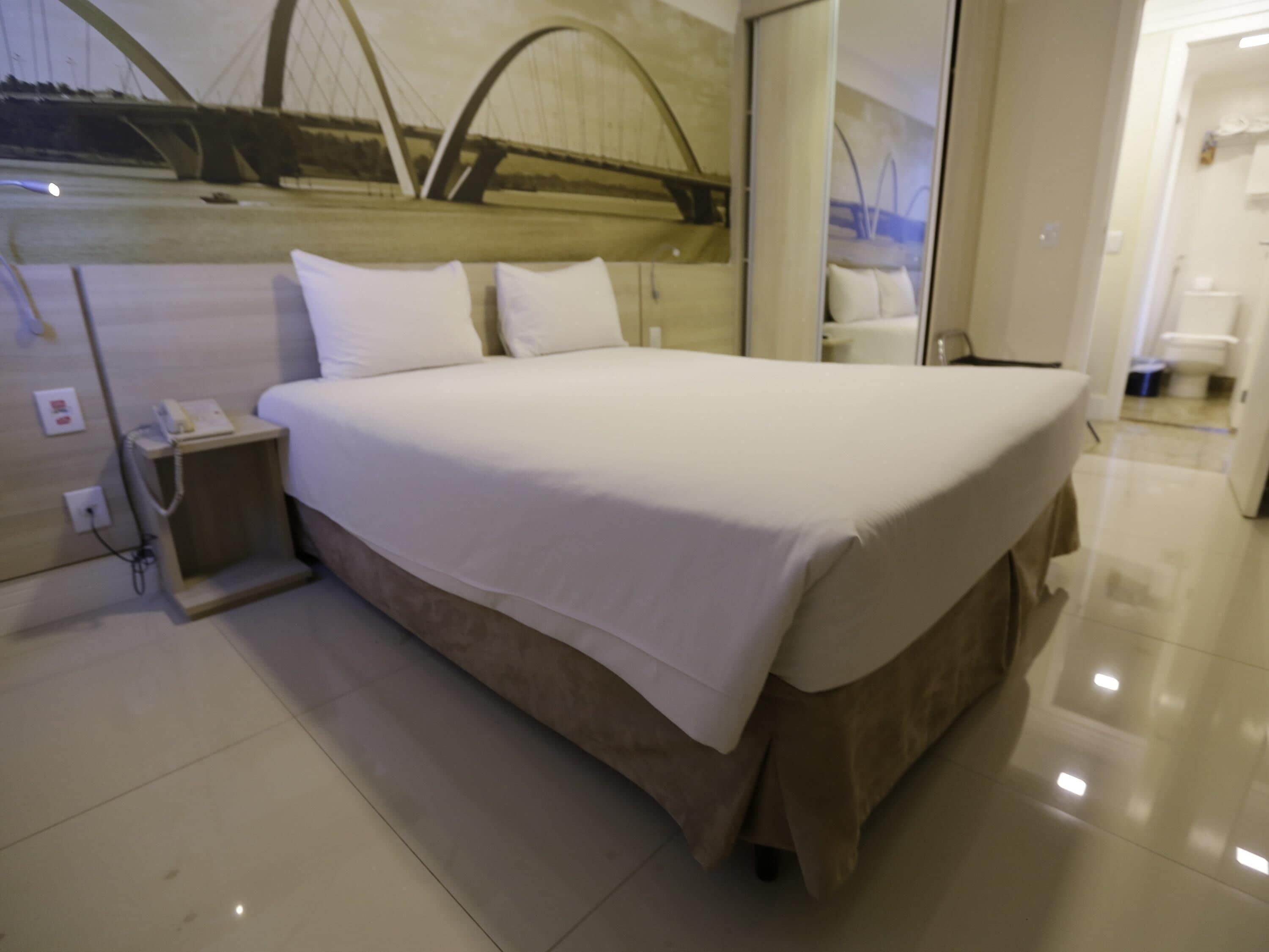 A hotel room with a bed, a nightstand, a phone, and a view of a bridge.