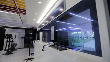 A modern hotel lobby with a reception desk, a treadmill, and a glass wall offering a view of the outside.