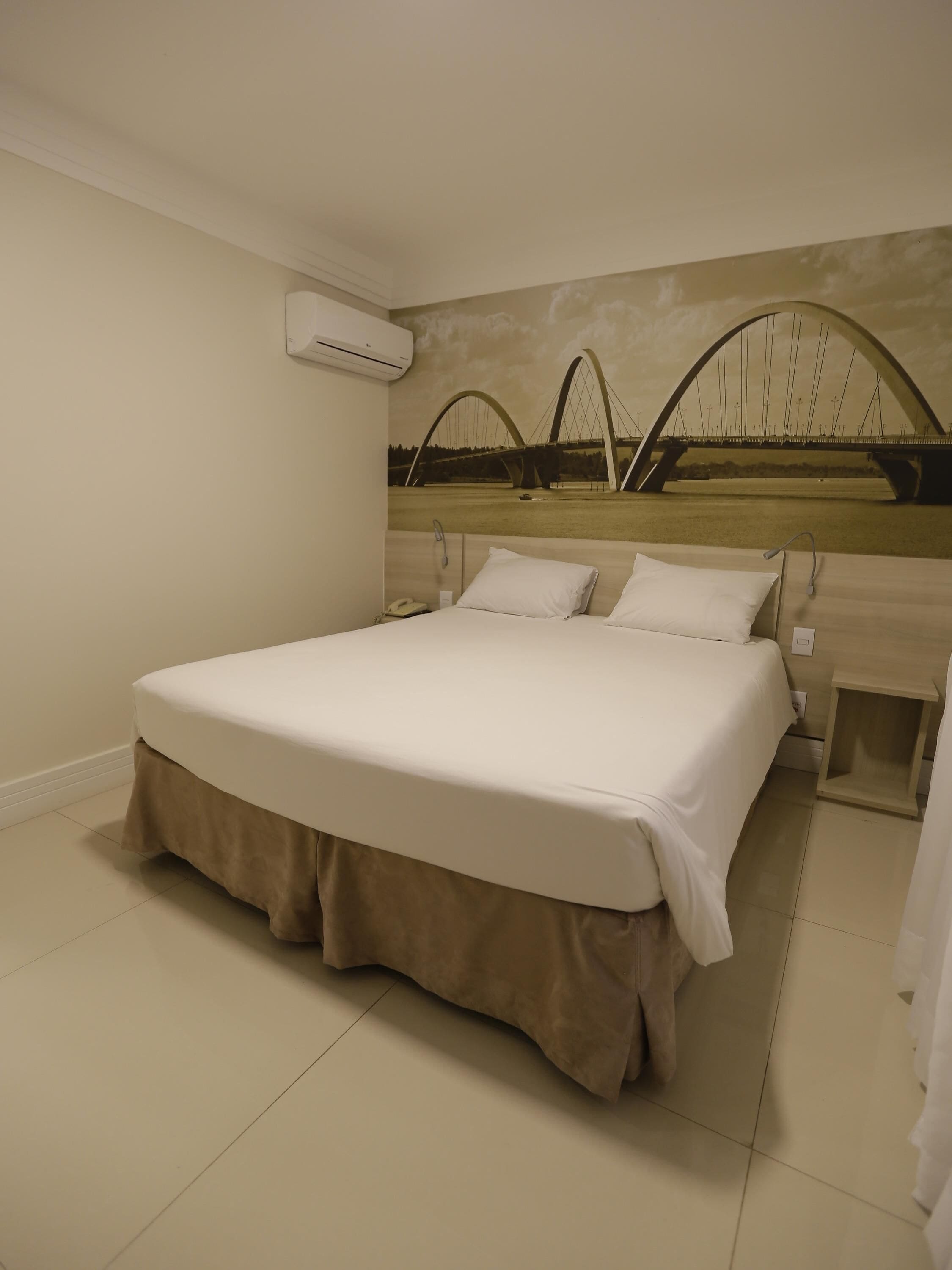 Habitación de hotel con una cama grande, un equipo de aire acondicionado, una mesita de noche y un mural en la pared de un puente.