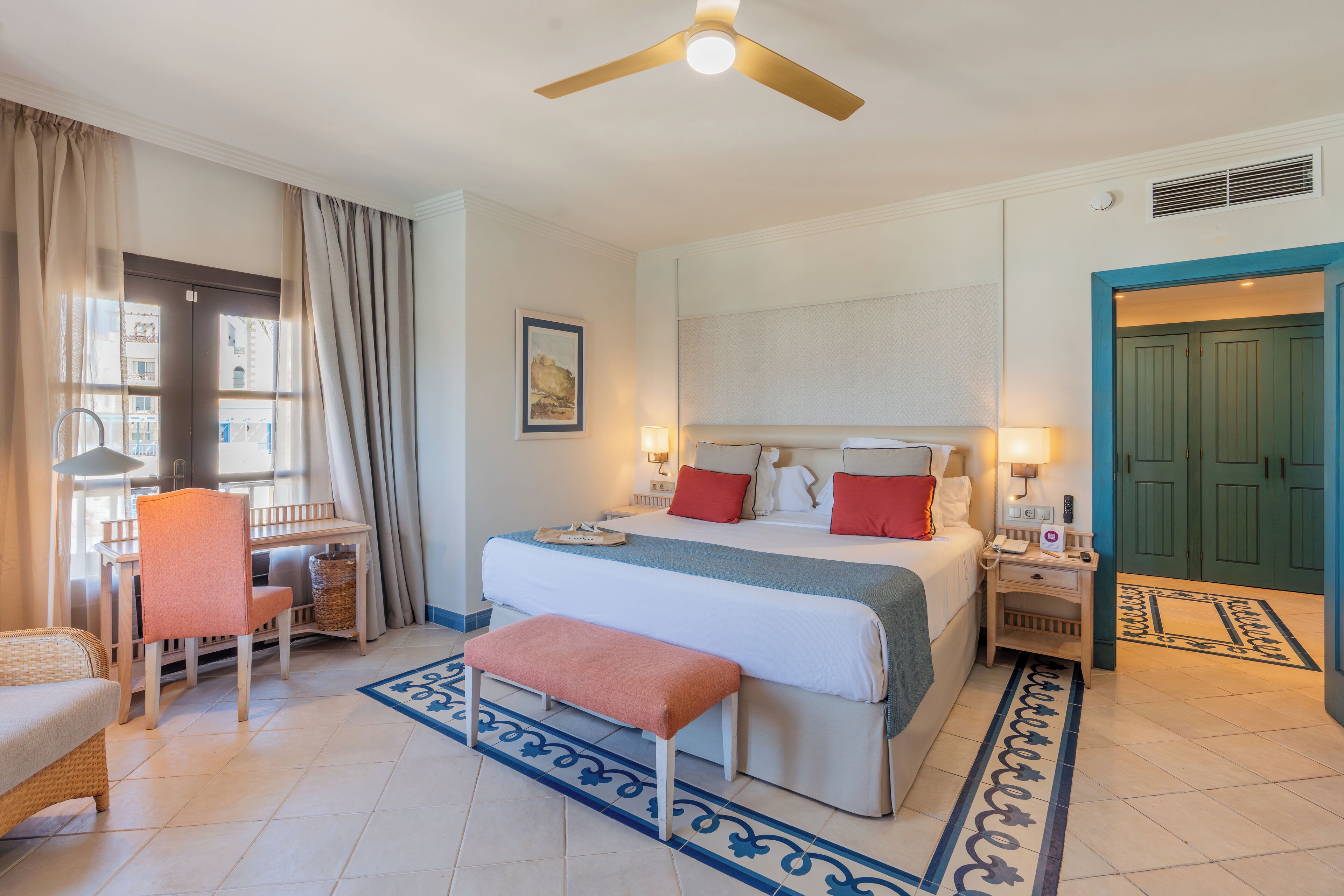 Habitación de hotel con cama, mesita de noche, silla, escritorio y ventilador de techo.