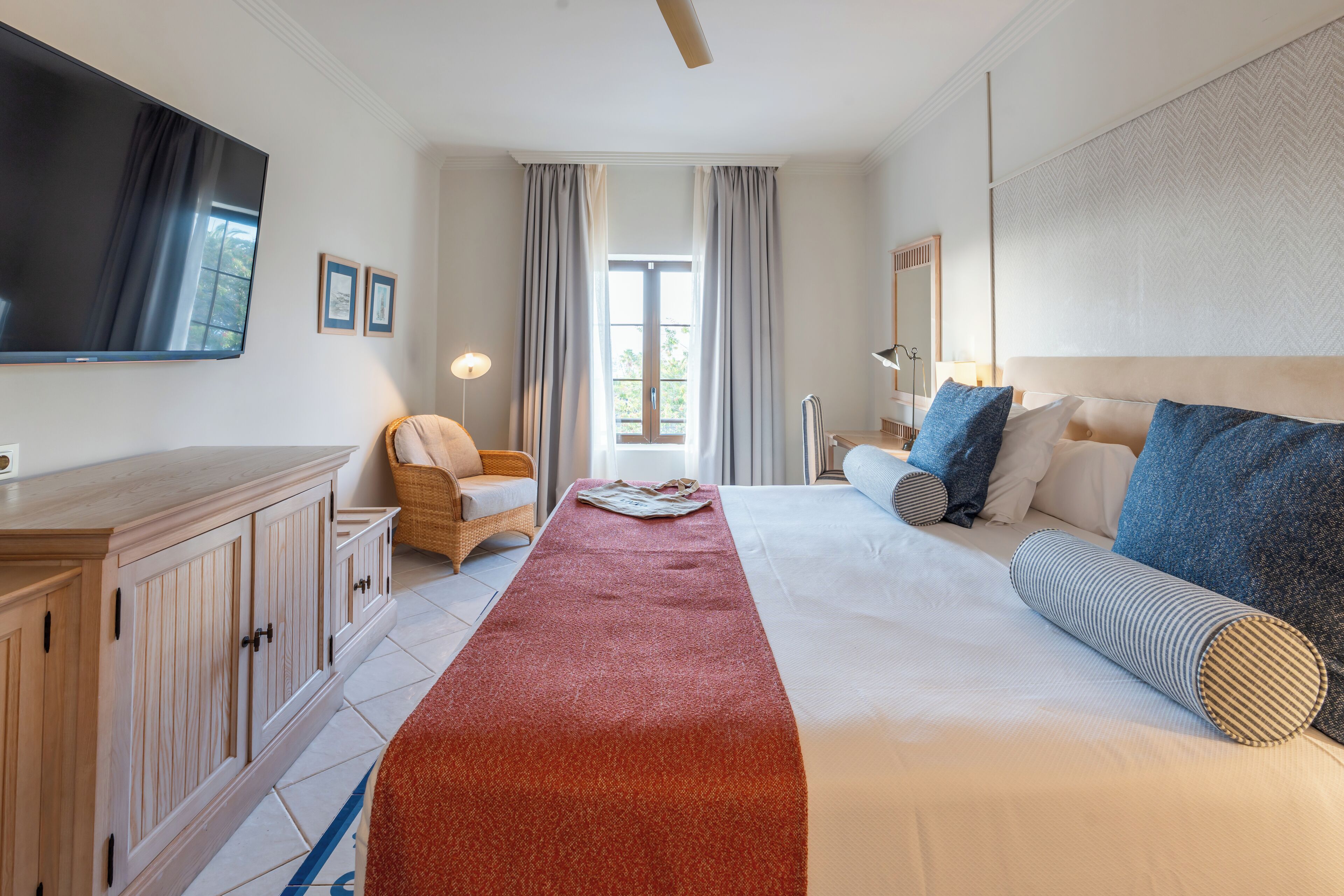 A hotel room with a large bed, a flat-screen TV, a wooden cabinet, a chair, and a view of the outdoors through a window.