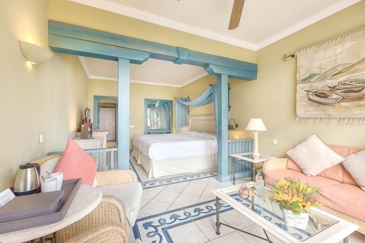 Habitación de hotel con cama, zona de estar con mesa y sillas, sofá y ventana grande.