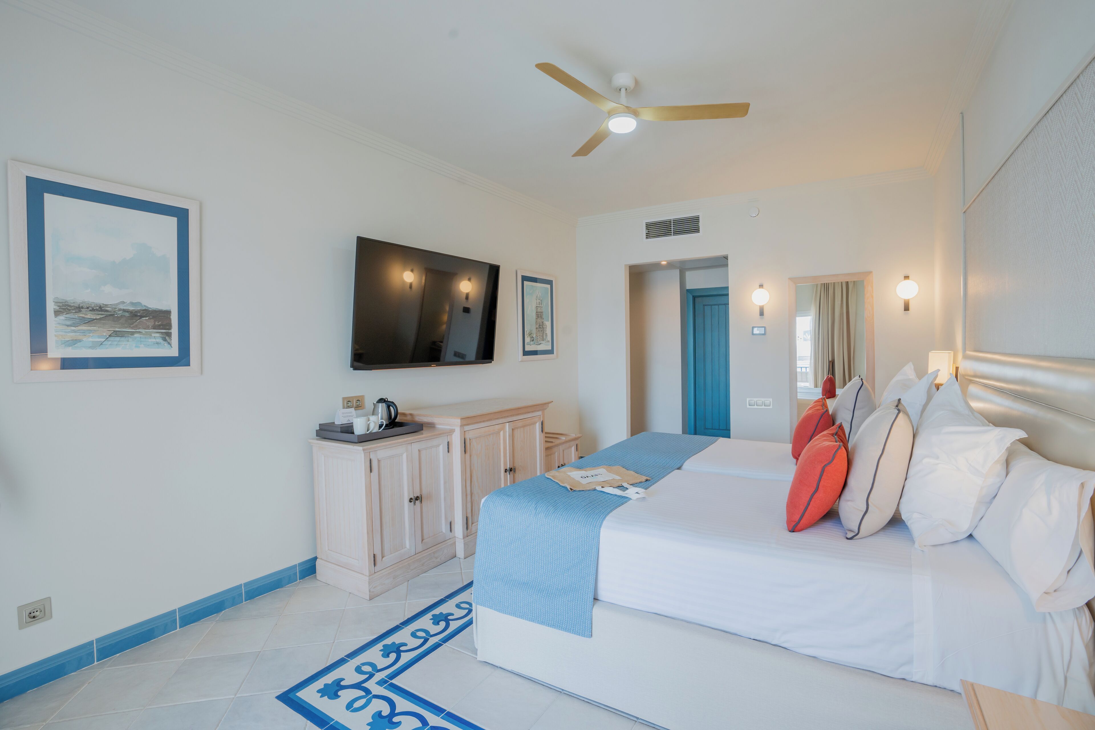 A hotel room with a bed, a television mounted on the wall, a wardrobe, and a bathroom door visible in the background.