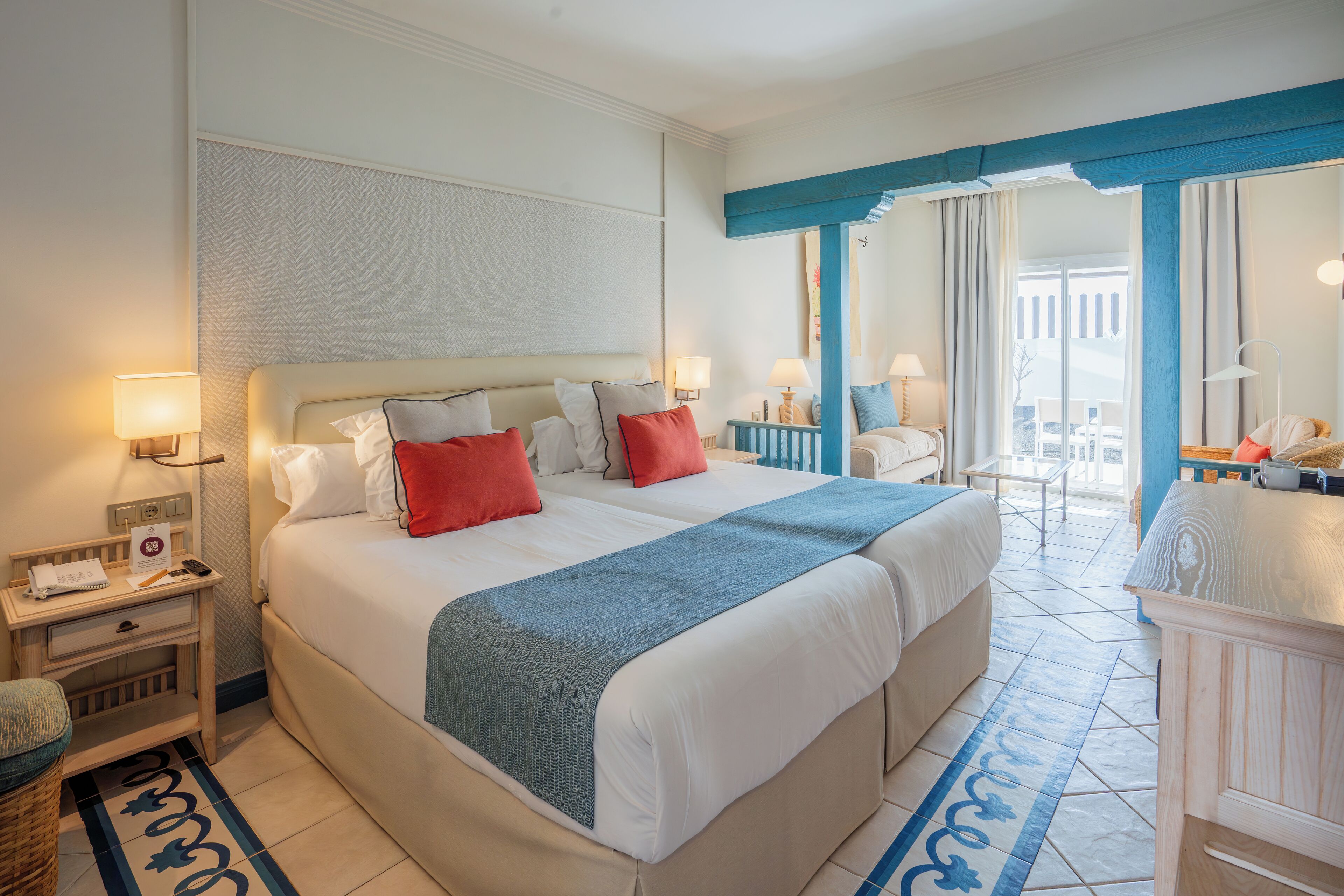 A hotel room with a large bed, two bedside tables, a nightstand, a chair, and a balcony with a view.