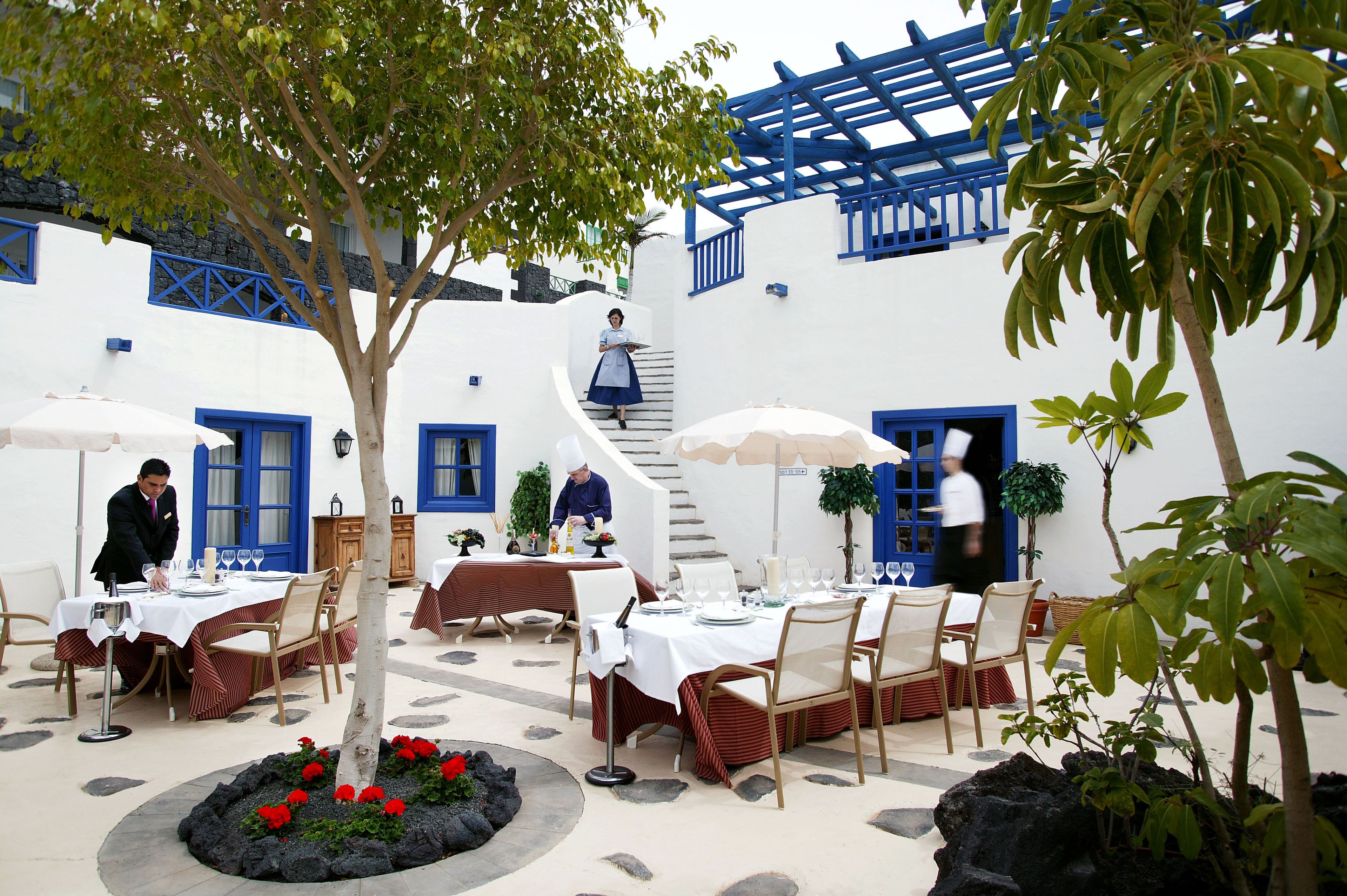 A courtyard with outdoor dining tables, a staircase, and a tree.