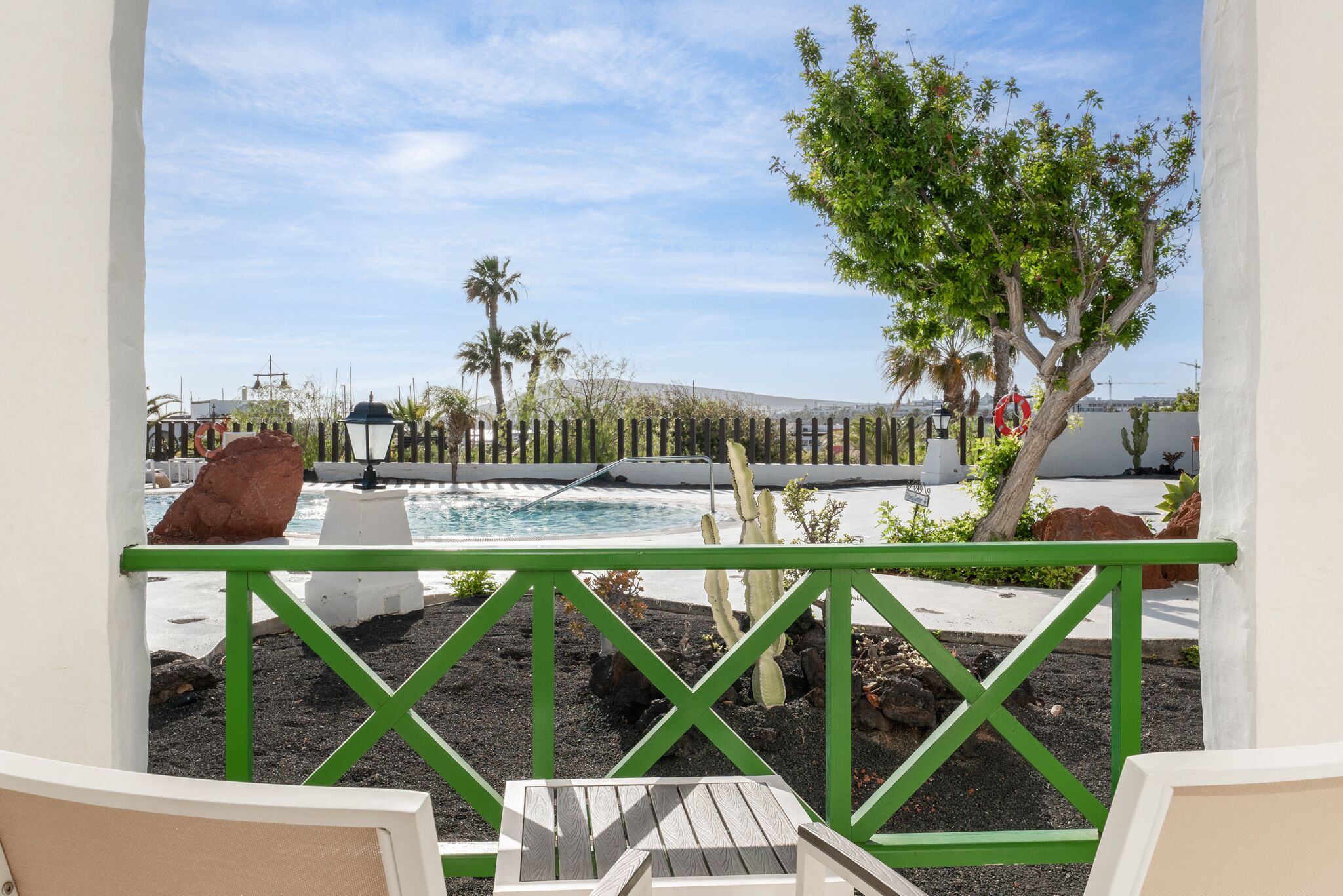A poolside area with a view of a pool, lounge chairs, and a cactus plant.