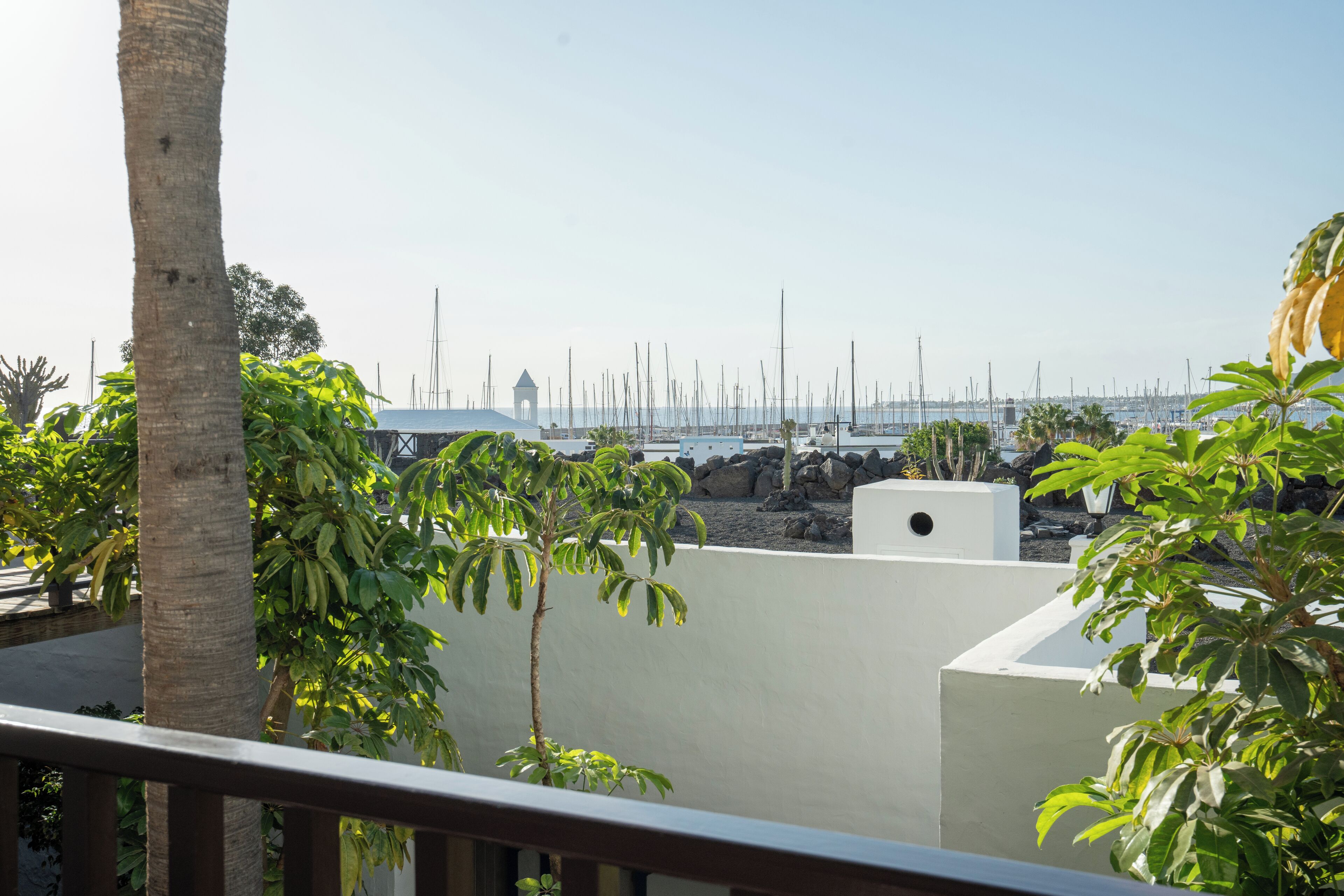 A balcony with a view of a marina, palm trees, and a white building with a tower.