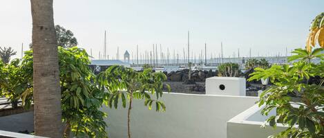 A balcony with a view of a marina, palm trees, and a white building with a tower.