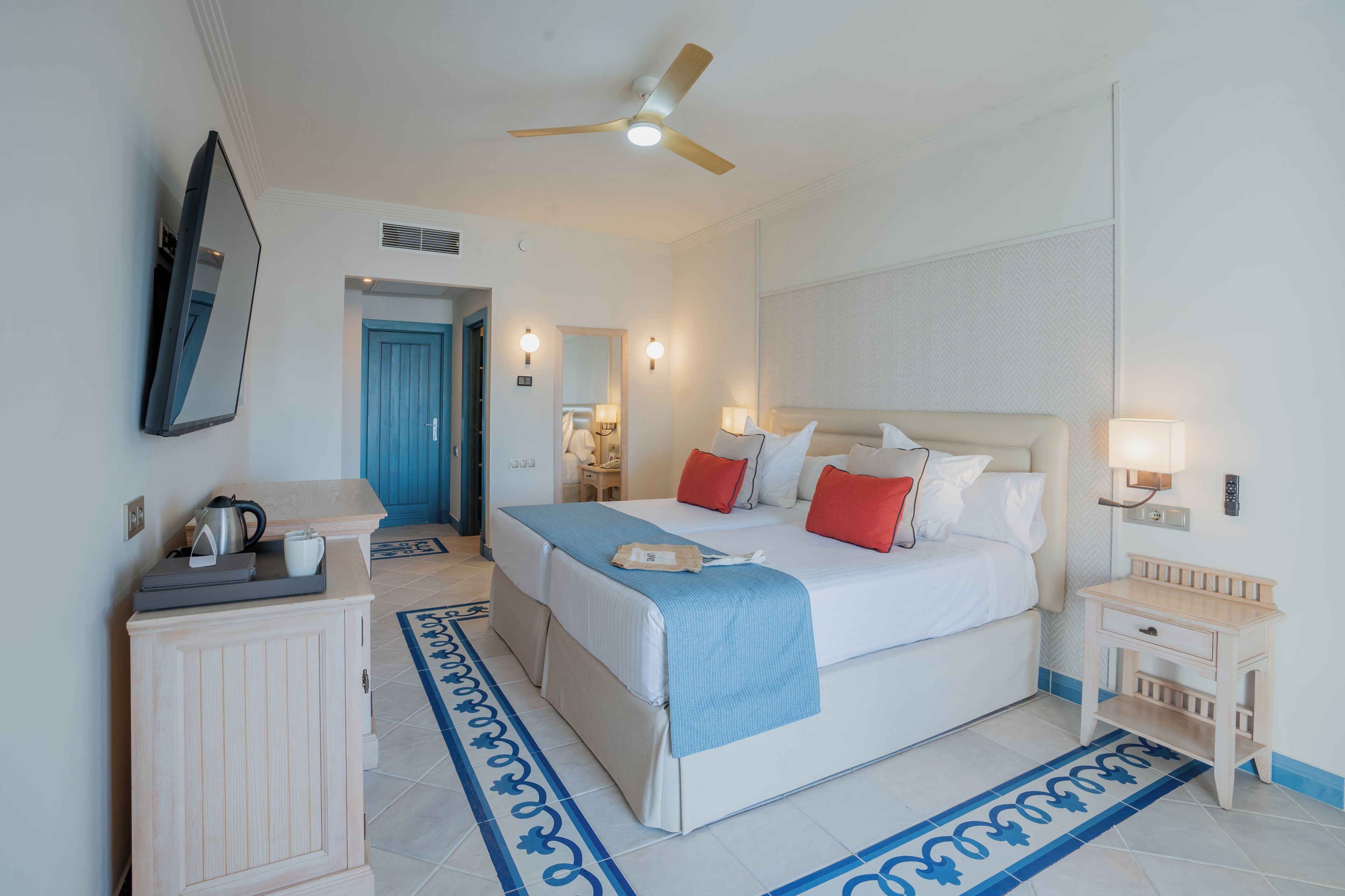 Une chambre d’hôtel comprenant un lit, une table de chevet, une commode et un bureau avec un miroir et une bouilloire.
