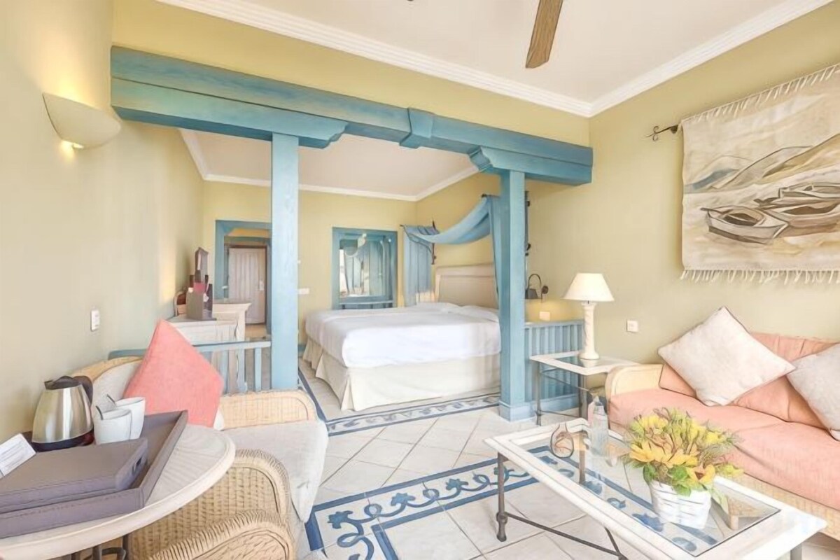 Habitación de hotel con cama, zona de estar con mesa y sillas, un sofá y un ventanal grande.