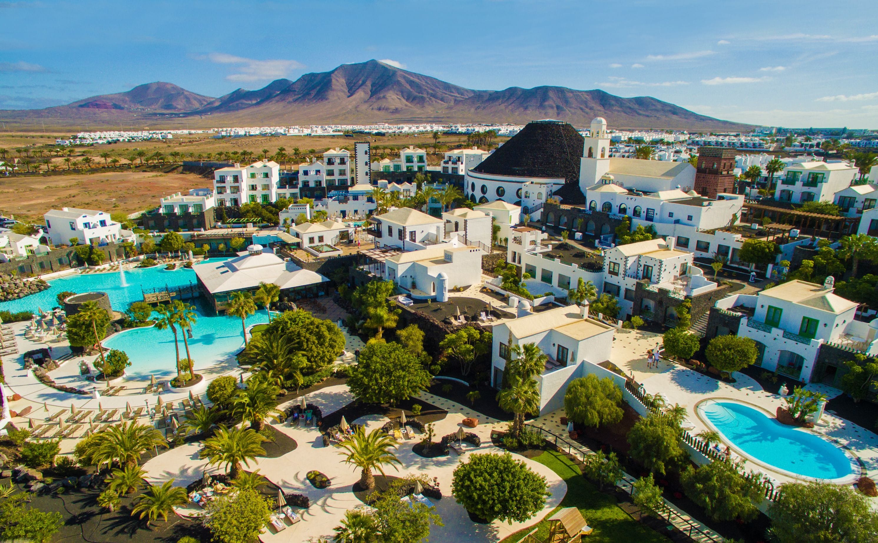 Resort com várias piscinas, palmeiras e montanhas ao fundo.