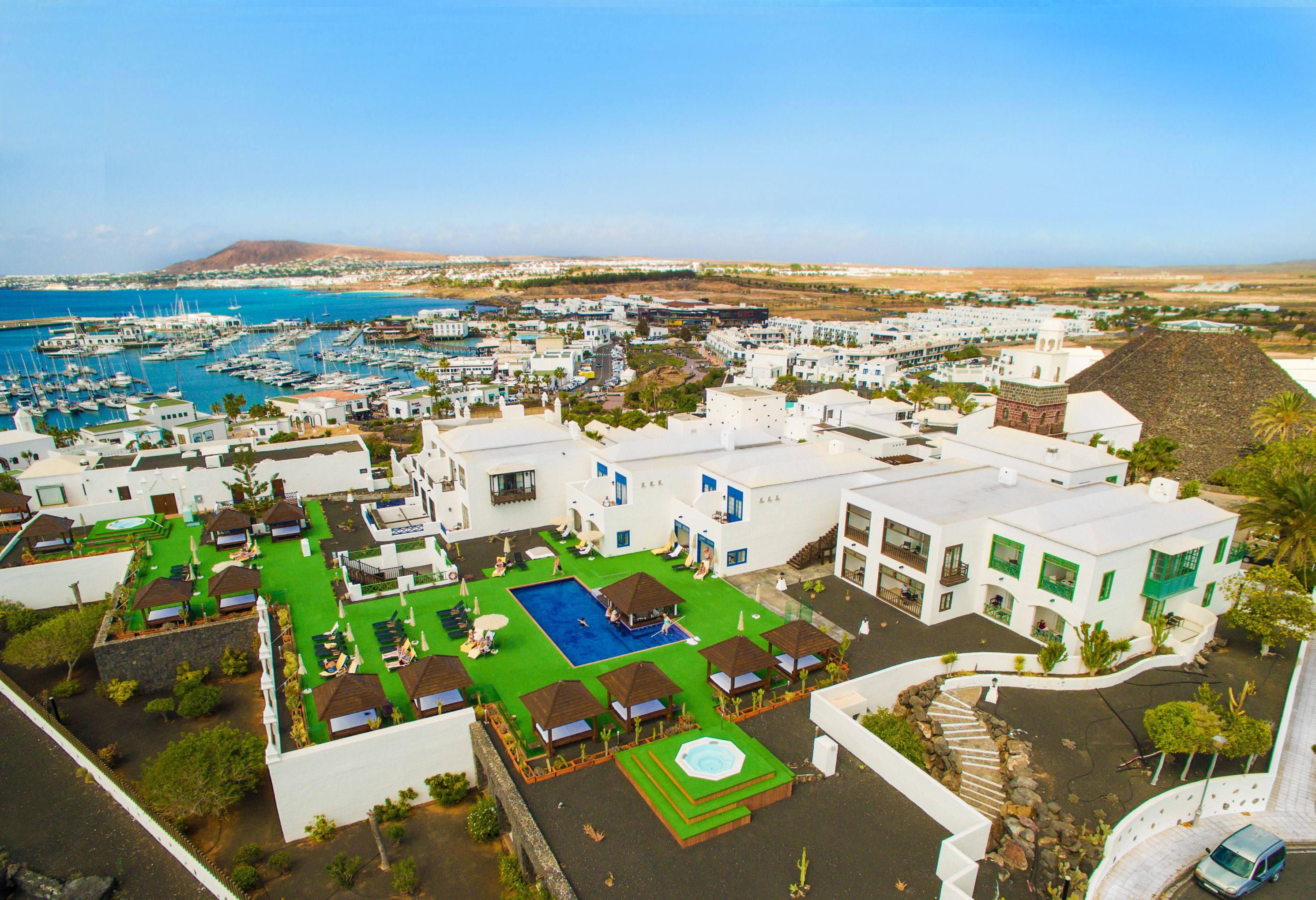 Un complejo turístico frente al mar con un puerto deportivo, piscina y varias edificaciones con balcones.