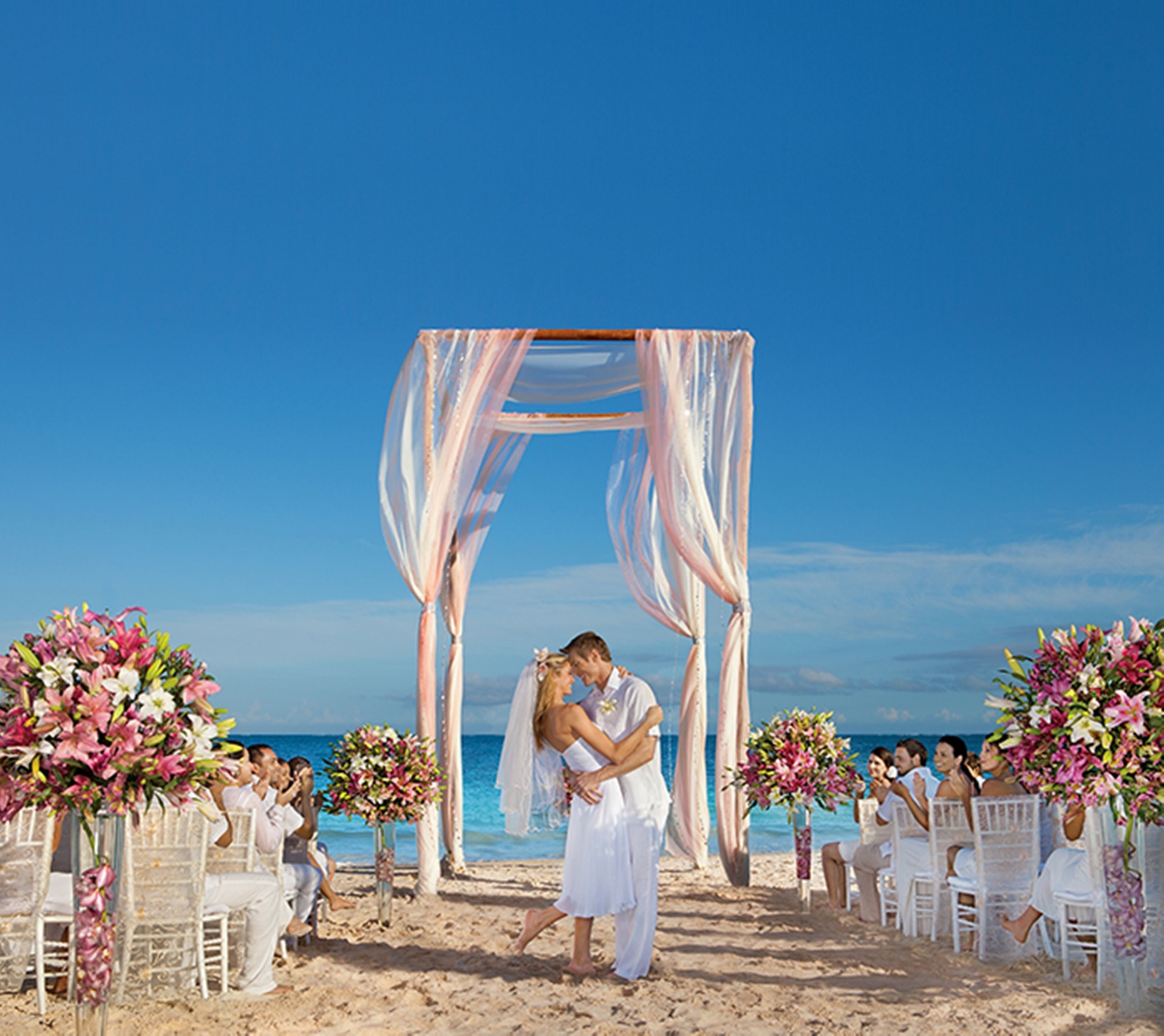 Une cérémonie de mariage sur la plage, avec une arche blanche et des décorations florales.