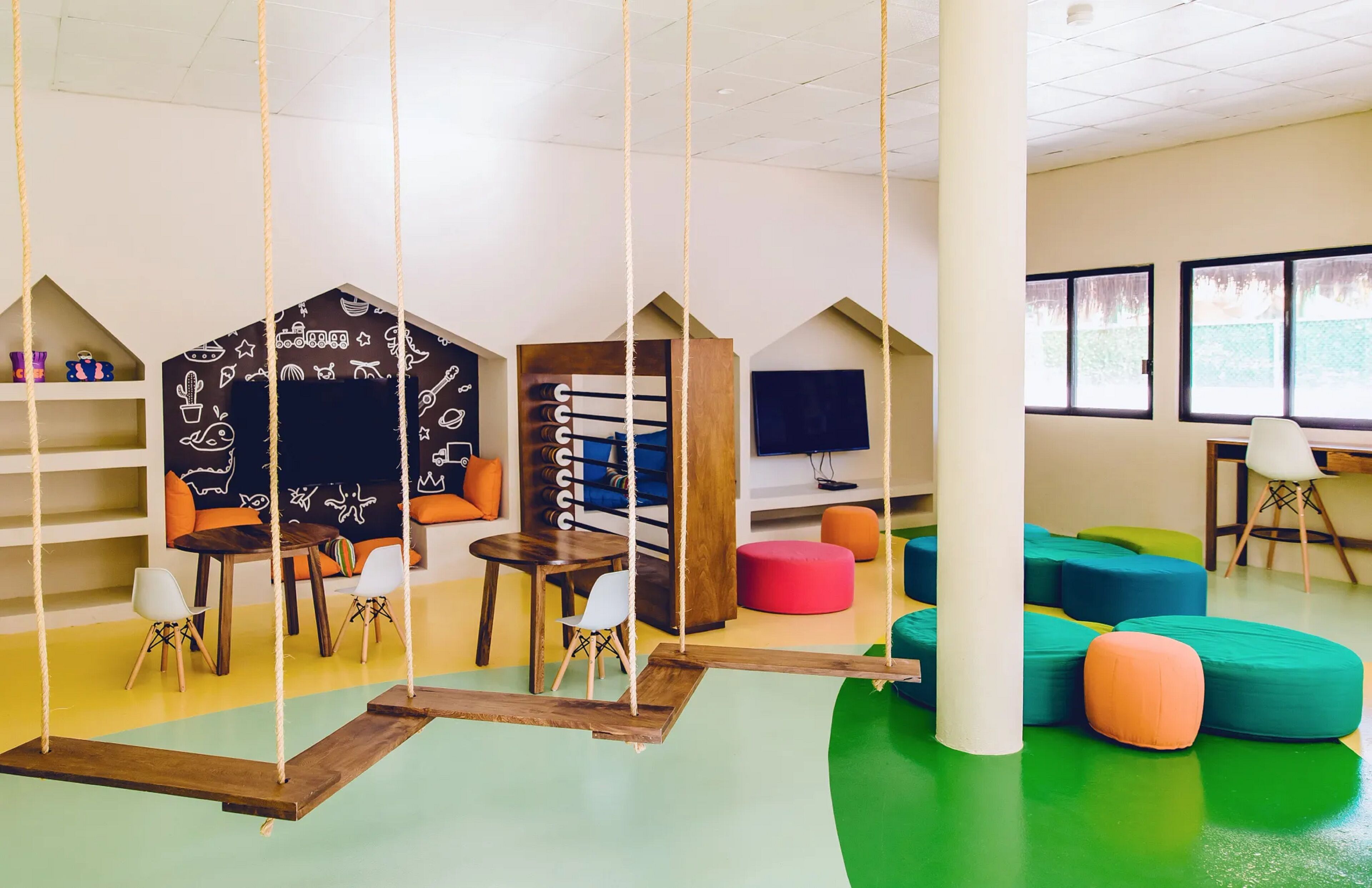 A children's playroom with colorful furniture, a swing set, and educational decorations.