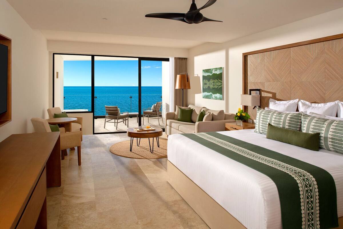 Een hotelkamer met een groot bed, een bureau, een stoel, een kleine tafel en uitzicht op de oceaan.