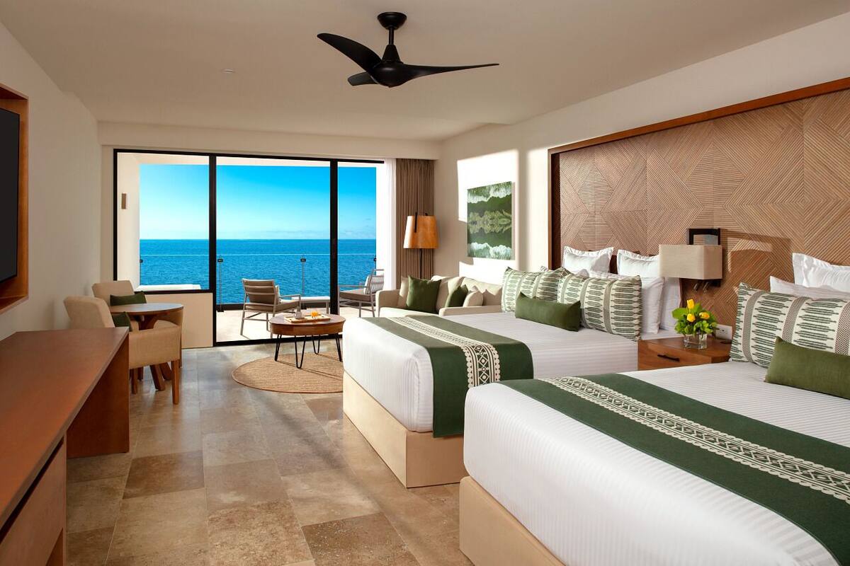 Een hotelkamer met twee bedden, een bureau, een stoel en uitzicht op de oceaan.
