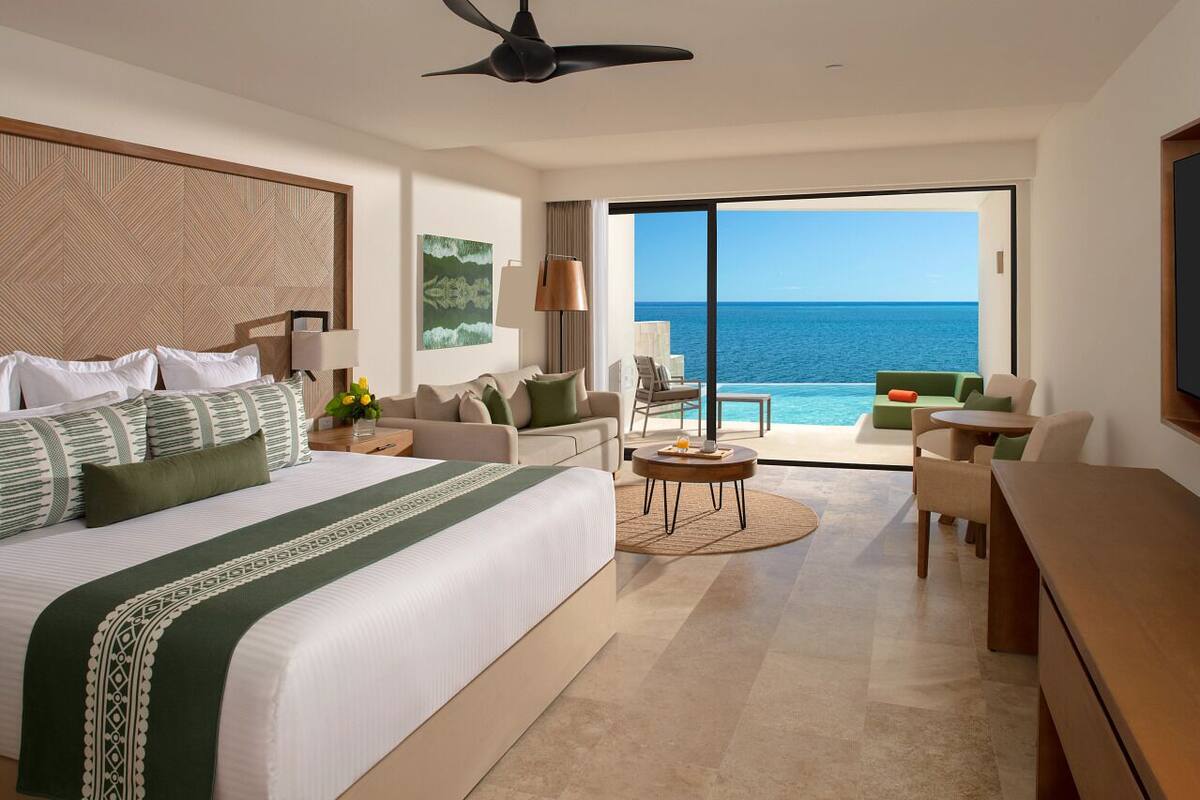 Een moderne hotelkamer met een groot bed, een bank, een zithoek en een balkon met uitzicht op de oceaan.