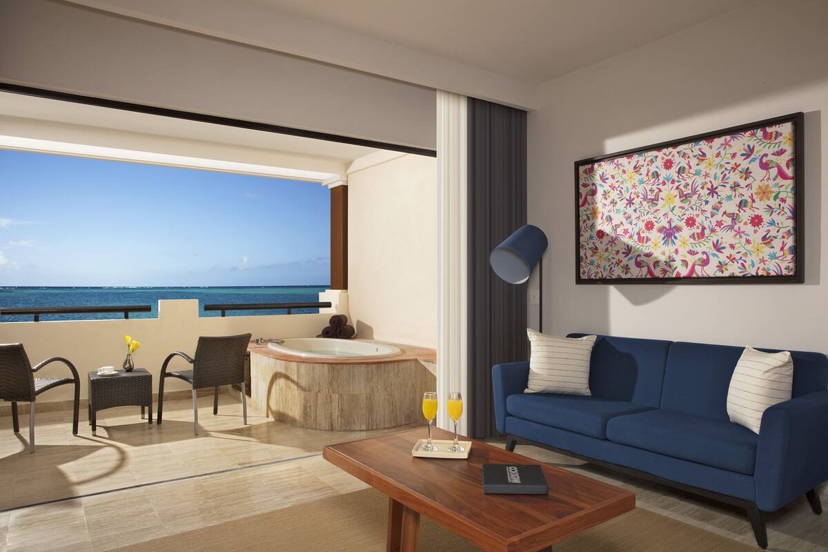 Een moderne hotelkamer met een balkon, een blauwe bank, een bijzettafeltje en een schilderij.
