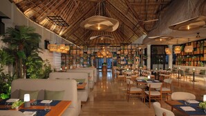 Ein geräumiges Restaurant mit hohen Decken, Holzbalken und hängenden Pendelleuchten. Die Tische sind mit weißen Servietten und Gläsern gedeckt.