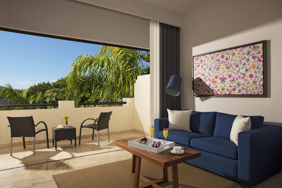 Een moderne woonkamer met een blauwe bank, een houten salontafel en een balkon met twee stoelen en een klein tafeltje.