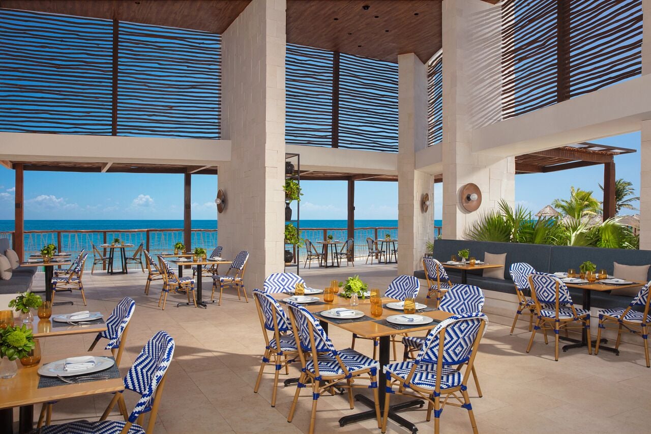 Un espacio de comedor al aire libre con mesas y sillas, con vista al mar.