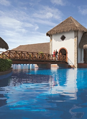 A pool area with a wooden bridge connecting to a building with a thatched roof.