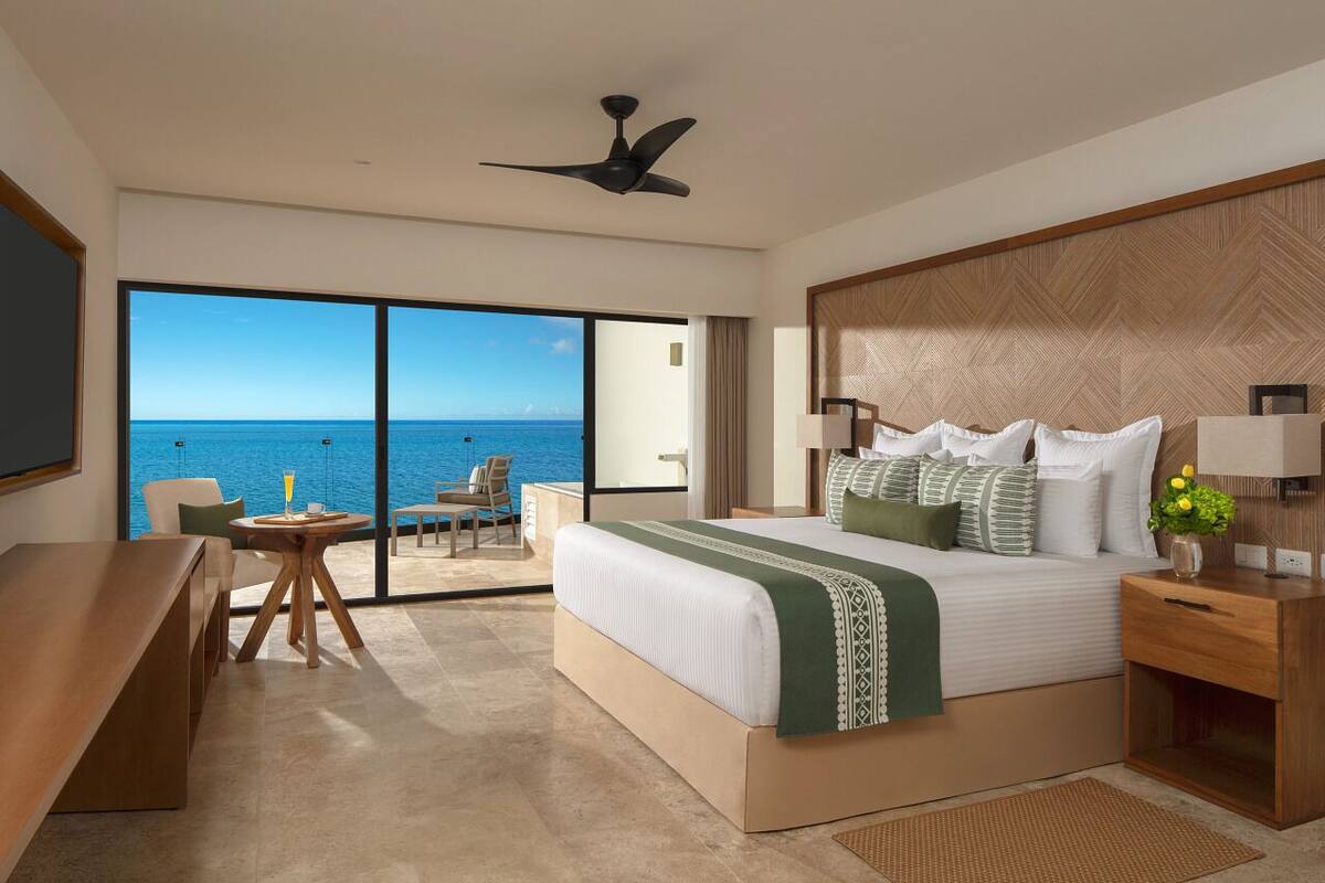 Een hotelkamer met een groot bed, een bureau, een stoel en uitzicht op de oceaan.