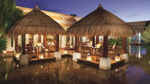 Un complexe hôtelier de luxe doté de bungalows sur pilotis aux toits de chaume, d’une piscine et d’un éclairage d’ambiance.