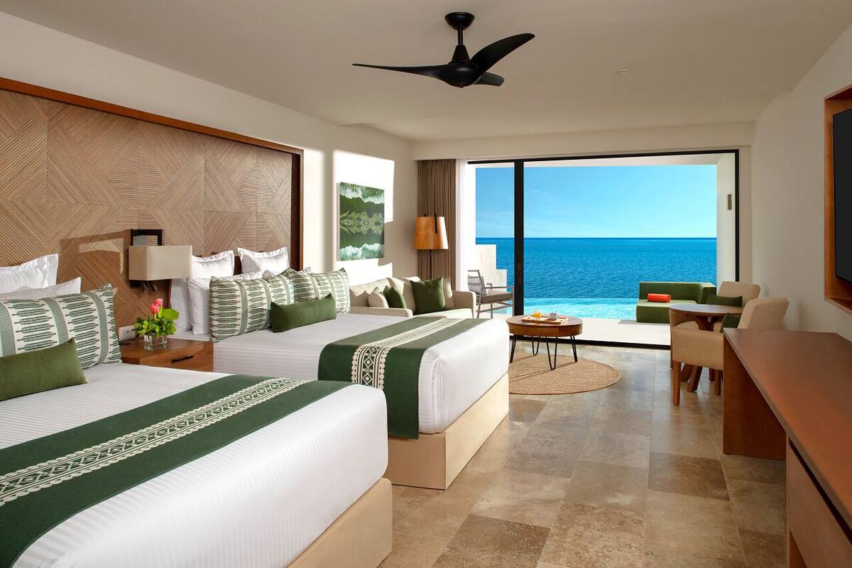 Een hotelkamer met twee bedden, een bureau, een stoel, een tafel en uitzicht op de oceaan.